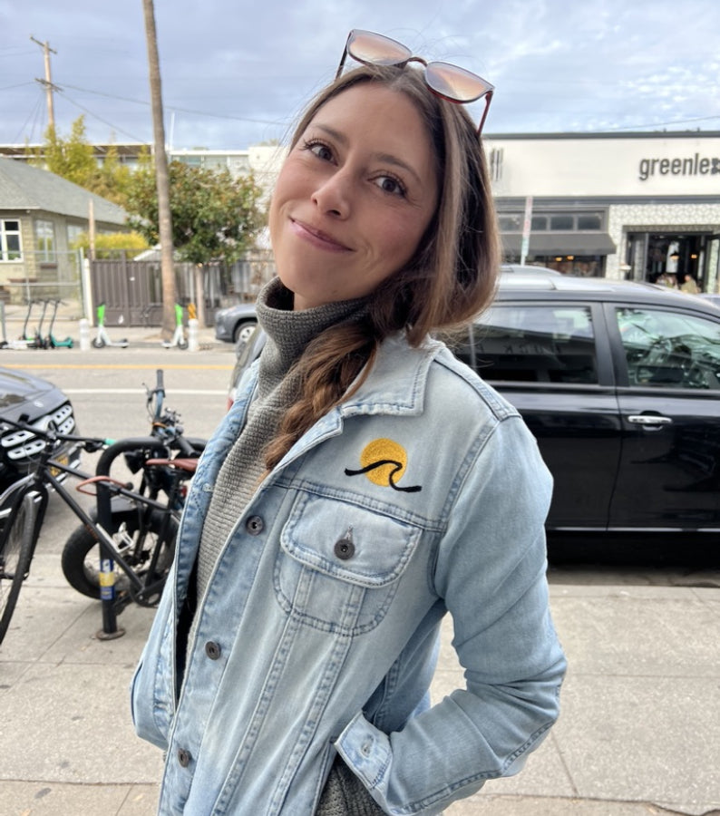 Woman wearing a light-wash denim jacket with a small custom chainstitch embroidered chest design by amR in Los Angeles