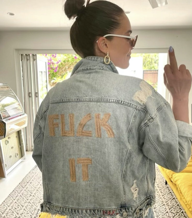 Custom chainstitch embroidery on a vintage-style distressed denim jacket, featuring oversized gold-toned FUCK IT lettering with raised textured stitching, frayed details and a bold statement back design by amR
