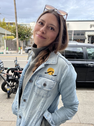 Woman wearing a light-wash denim jacket with a small custom chainstitch embroidered chest design by amR in Los Angeles