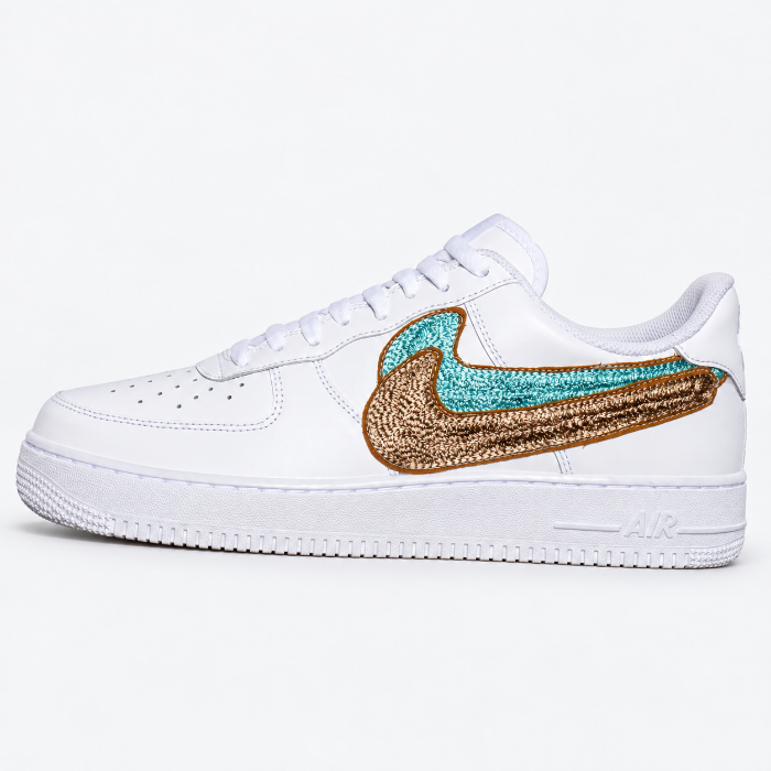 Custom chainstitch embroidery by amR on a white Nike Air Force 1 leather sneaker, featuring layered turquoise and metallic bronze-gold Swoosh designs with raised textured stitching and detailed embroidered outlines.