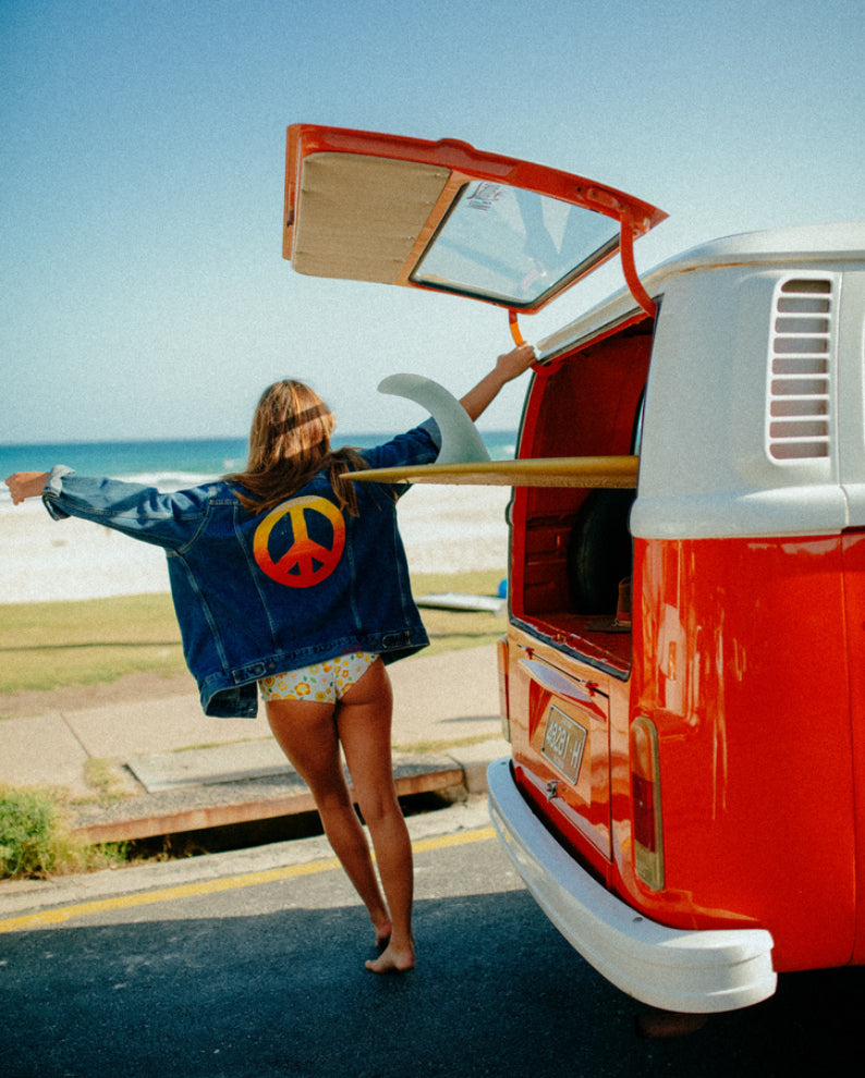Custom embroidered denim jacket with a colorful peace sign back design photographed by the beach in Los Angeles