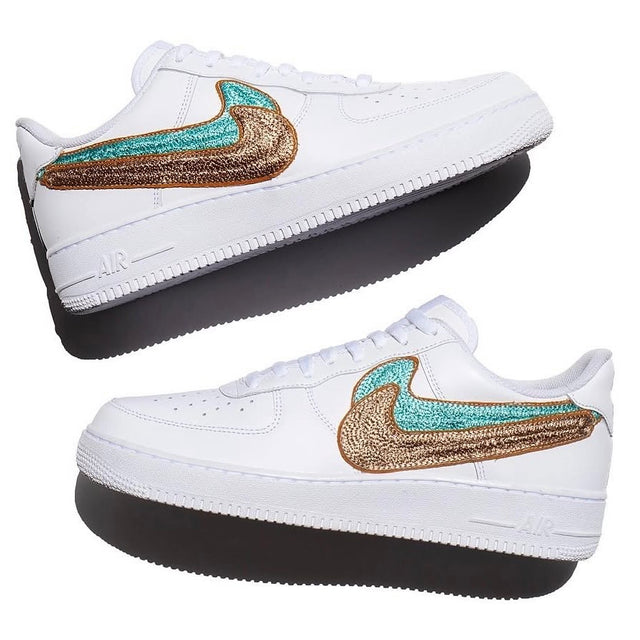 Custom embroidered white Nike Air Force 1 Low sneakers featuring oversized turquoise and metallic bronze-gold Swoosh designs with intricate textured stitching, shown from both sides