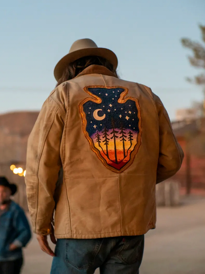 Custom embroidery on the back of a tan jacket with a colorful moon and forest design