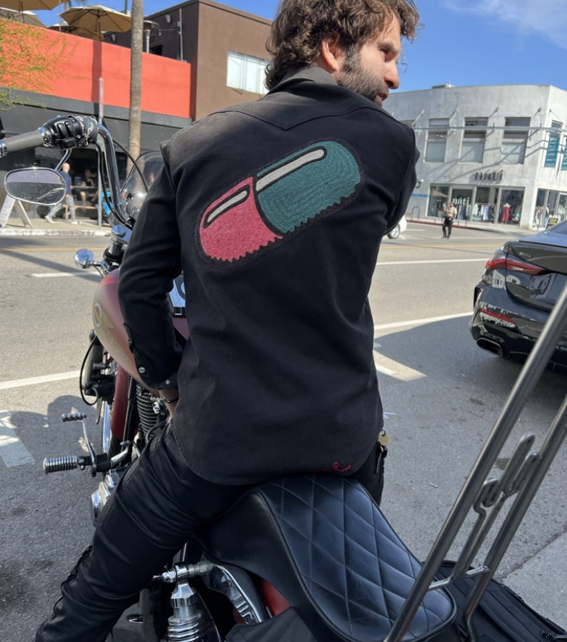 Man wearing a black shirt with large custom embroidered back artwork by amR while sitting on a motorcycle in Los Angeles
