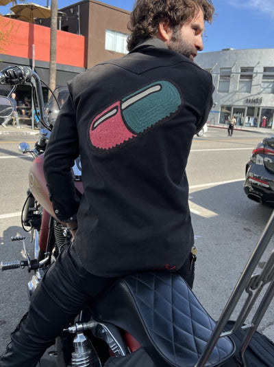 Man wearing a black shirt with large custom embroidered back artwork by amR while sitting on a motorcycle in Los Angeles